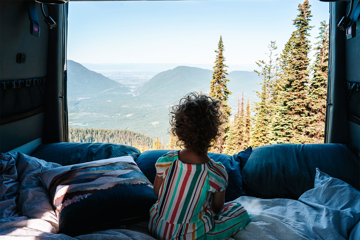 Young Girl Views Vast Valley Below from Bed of Moterra Campervan Rental in Glacier National Park, Montana
